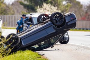 Highway vehicle rollover accident with police presence in the background.