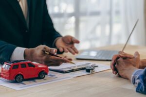 Salesman presenting car prices, interest rates, and insurance options to a customer at the desk in an office setting