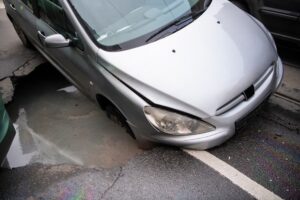 The car fell into a huge sinkhole on busy asphalt road surface on which cars drive. Accident situation on a city street due to cracks in asphalt. Broken hole with muddy water.